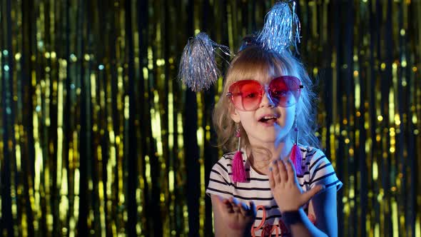 Stylish Teenager Kid Girl Standing on Backlit Blue Neon Lights and Points at Blank Space Agree Sign alt