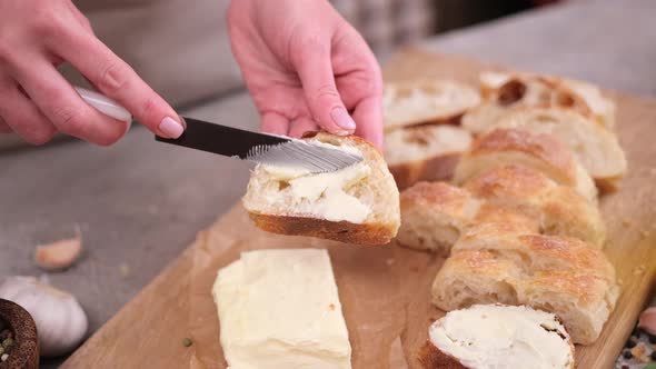 Woman Smearing Soft Butter on Slice of Baguette Bread By Knife at Domestic Kitchen alt