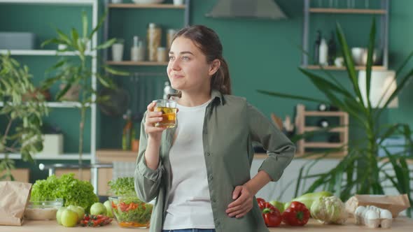 Happy Young Woman Enjoying Freshsqueezed Juice Using Organic Products in Modern Kitchen alt