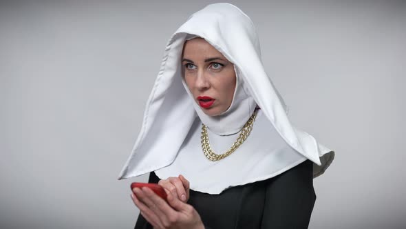 Positive Woman in Nun Costume Showing I Got an Idea Gesture Texting on Smartphone alt