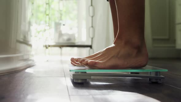 Woman checking her weight on weighing scale at home 4k alt