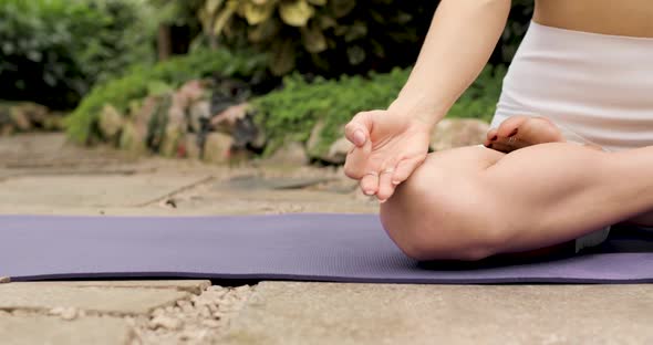 Closeup of Legs and Hands of a Woman Doing Yoga in the Lotus Position on a Mat in a Botanical Garden