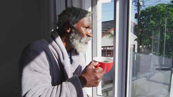 Senior man drinking coffee while looking out of window at home alt