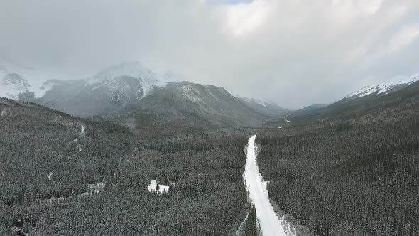 Drone approaching road through the forest at the foot of the beautiful mountains in Alberta, Canada alt