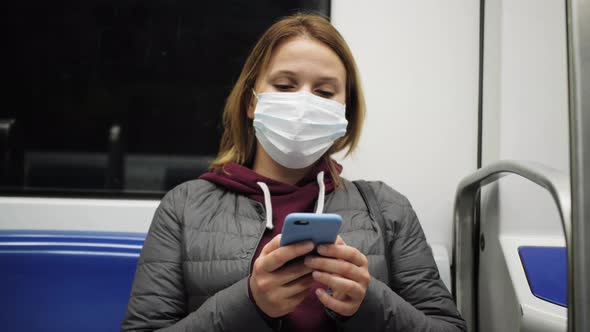 Young Woman in Protective Medical Face Mask in a Subway Train Using Mobile alt