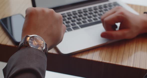 While Working On A Laptop, A Man Looks At His Watch So As Not To Be Late For A Meeting