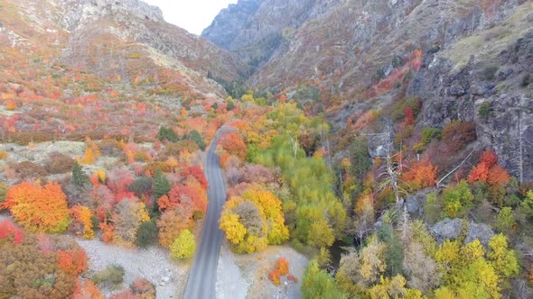 Aerial view flying backwards over road coming out of canyon during Fall. alt