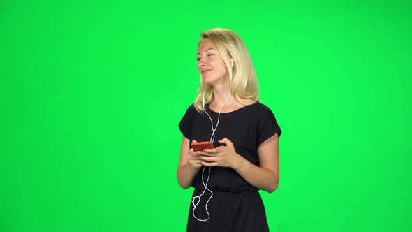 Attractive Girl Goes in Headphones and Texting with Smartphone. Chroma Key alt