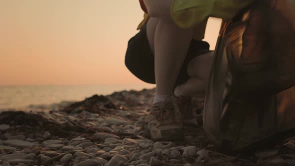 A female volunteer sits down and puts a plastic bottle in a plastic bag. alt