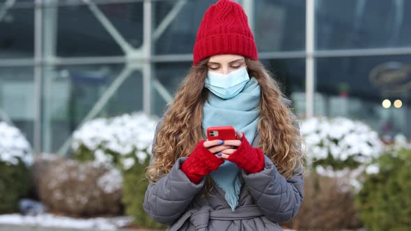 Curly Haired Woman in Protective Medical Mask Walks Down to the Street Uses Phone Texts Scrolls