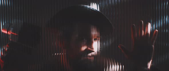 Man in shutter lights looking through clear panel holding hand up alt