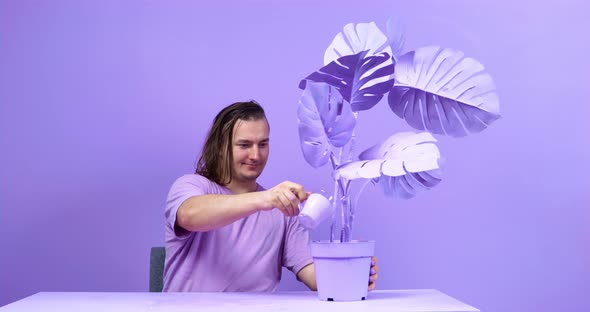 Young Man Takes Cup and Pours Paint Into Pot with Flower and Then Appraisingly Examines Plant While