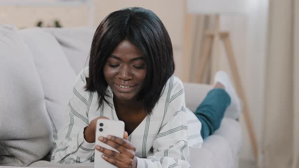 Young African American Woman Lying on Couch Resting Relaxing Chatting on Video Call Using Smartphone alt