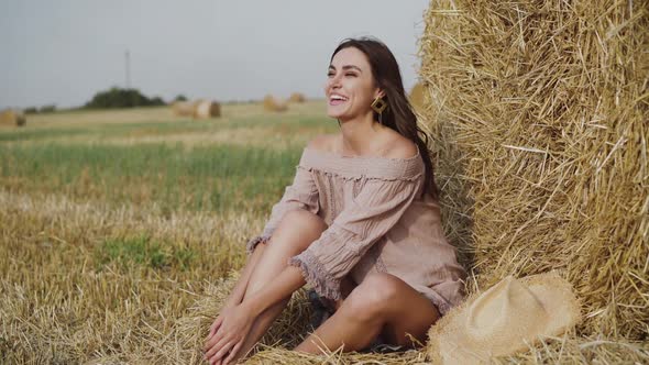 Woman in Summer Dress Resting at a Haystack in a Field and Talking with Laugh alt