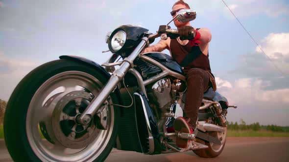 Stylish Biker with Tattoos Rides a Motorcycle on a Country Road at Sunset