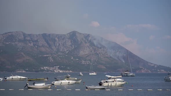 Sailboats Float in the Sea Against the Background of Smoke From Fires in Budva alt