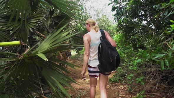 girl with a backpack travels through the rainforest. walking along the trail on the island alt
