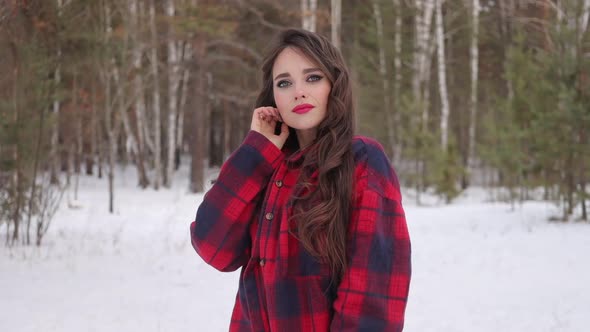 Young Woman with Wavy Hair Standing and Touching Face in Winter Forest