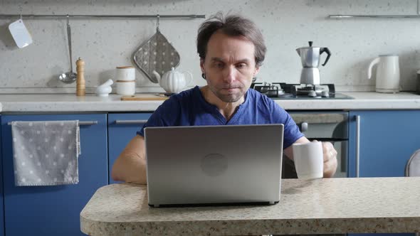 Male Freelancer Teleworking and Having Coffee While Sitting in the Kitchen