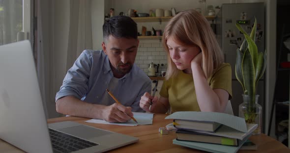 Young Dad Helping Teenage Daughter Schoolgirl Study Online at Home Sitting at Kitchen Table at Home alt