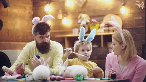 Happy Family Painting Eggs on Easter Holiday. Mother, Father and Son Child Wearing Bunny Ears. alt