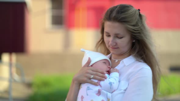 A Newborn Boy in His Mother's Arms While Walking Down the Street Near the House alt