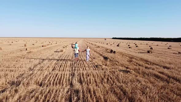 Family of Three Strolls Through a Mown Wheat Field on a Sunny Summer Day