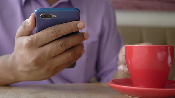 Close Up of Young Man Hand Using Smart Phone and Drinking Coffee at Cafe alt