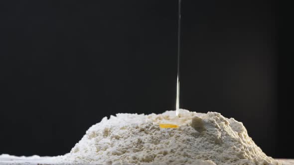 Egg with Yolk Falls Down Into Hole in White Flour on Table alt