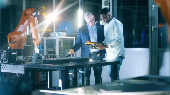 Two Male Scientists Are Using an Electronic Device To Operate a Robot alt