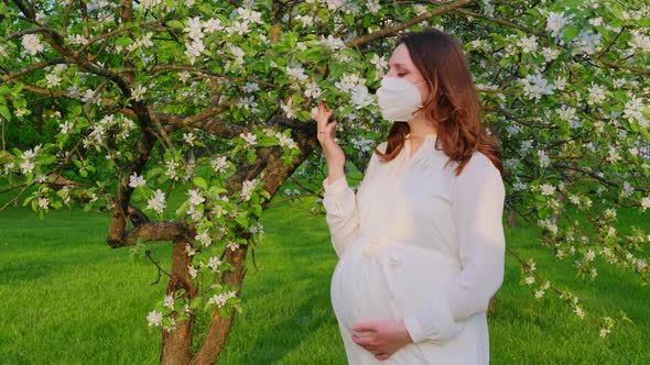 Pregnant woman in medical face mask n95 with apple tree flowers in spring nature