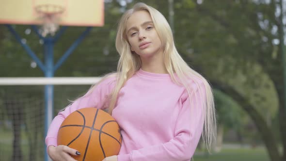 Middle Shot of Young Confident Basketball Player Posing with Ball Outdoors. Portrait of Happy alt