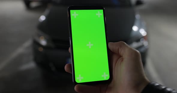 Mockup of male hand holding green screen of smartphone connected with car put it on alarm alt