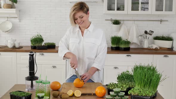 Young Woman Cuts an Orange to Make a Smoothie