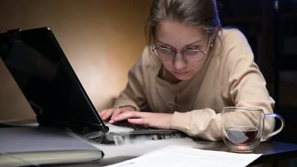 A young woman's old laptop starts to smoke while she is working alt