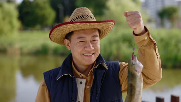 Close View of the Asian Man Wearing Special Fishing Clothes Holding the Fish He Caught on the Hook alt