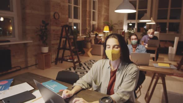 Portrait of Woman in Face Mask Working at Desk in Loft Office alt