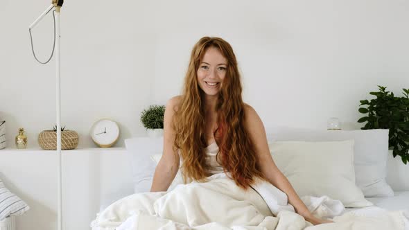 Portrait of a happy smiling woman in pajamas on a bed  in white bedroom