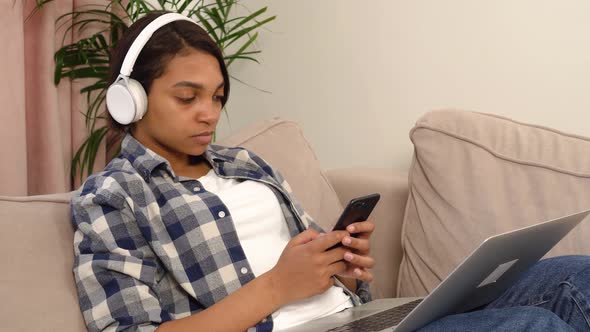 An AfricanAmerican Woman with Headphones Listens to Music While Lying at Home