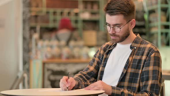 Focused Young Man Doing Paperwork in Cafe  alt