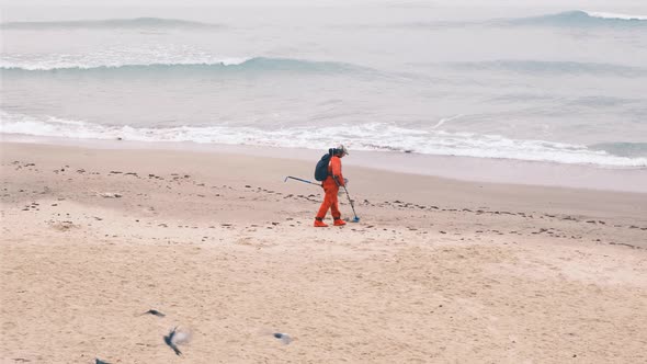 Man is Looking for the Lost Luxuries with Electronic Metal Detector on the Beach on a Cloudy Fall