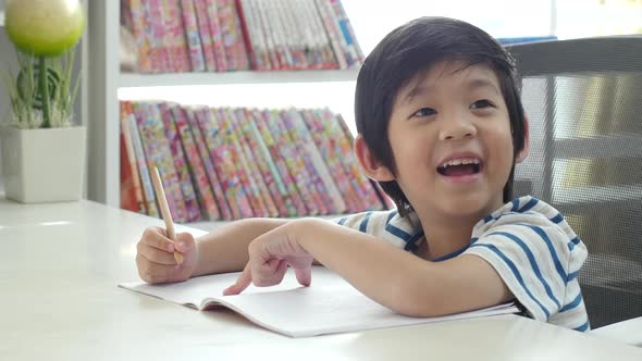 Little Asian Child  Using A Pencil To Write On Notebook At The Desk alt
