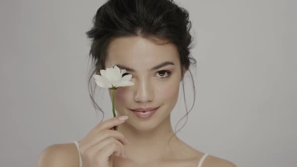Cute Girl Closing Eye with Camomile Flower and Smiling To Camera