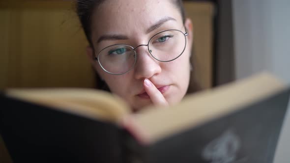 girl with glasses reading a book, view from behind the book, close-up alt