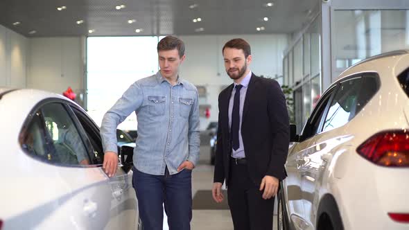 Caucasian Professional Auto Dealer and Young Customer Are Discussing New Car. alt