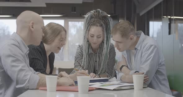 Group of Four Millennial Young People Discussing Project in Office Turning To Camera and Smiling alt