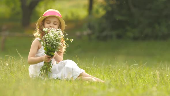Child Holds a Bouquet of Wildflowers in Her Hands, She Smells Them and Smiles alt
