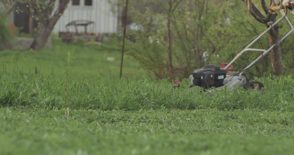 Green Grass in the Garden and Man with a Lawn Mower in Slow Motion is Passing By alt