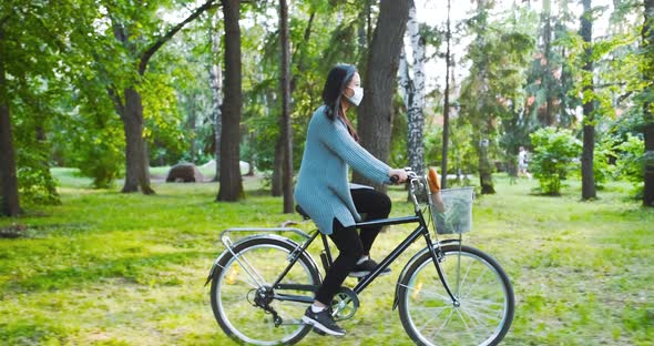 Riding a bike in park, cycling during quarantine. Girl in mask drives bicycle carrying food