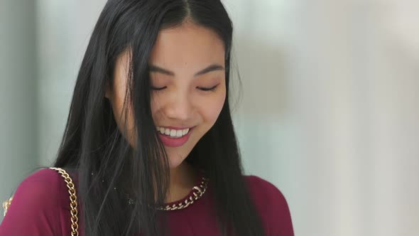 Close up of Asian woman looking at her phone and smiling then looking around then looking back at he alt